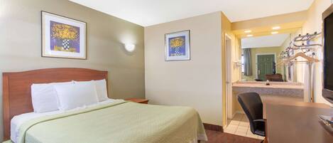 A hotel room with a bed, a desk, and a chair. There are two framed pictures on the wall.