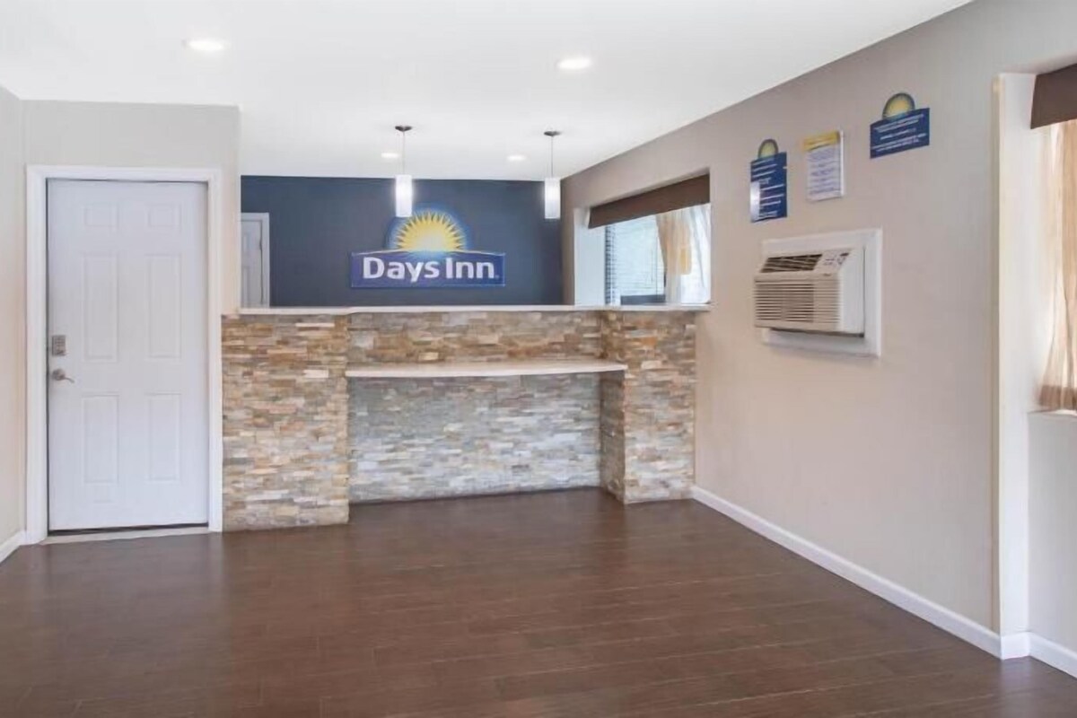 Un vestíbulo de hotel con el letrero de Days Inn, una chimenea de piedra, un equipo de aire acondicionado y una puerta.