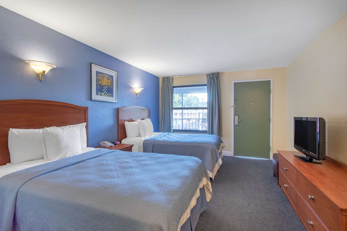 A hotel room with two beds, a TV, a desk, and a window with curtains.