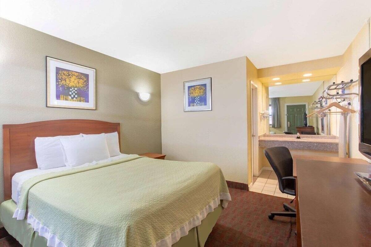 A hotel room with a bed, a desk, a chair, and two framed pictures on the wall.