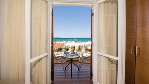 Un balcón con mesa y sillas, con vista a una playa con sombrillas y cielo despejado.