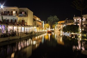 Vista nocturna de un canal flanqueado por edificios, incluyendo un restaurante con terraza y un puente al fondo.