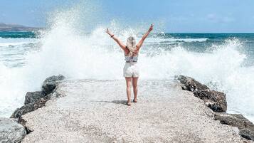 A person standing on a rocky pier with waves crashing behind them.