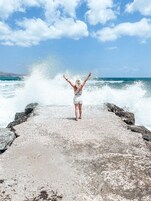 A person standing on a rocky pier with waves crashing behind them.