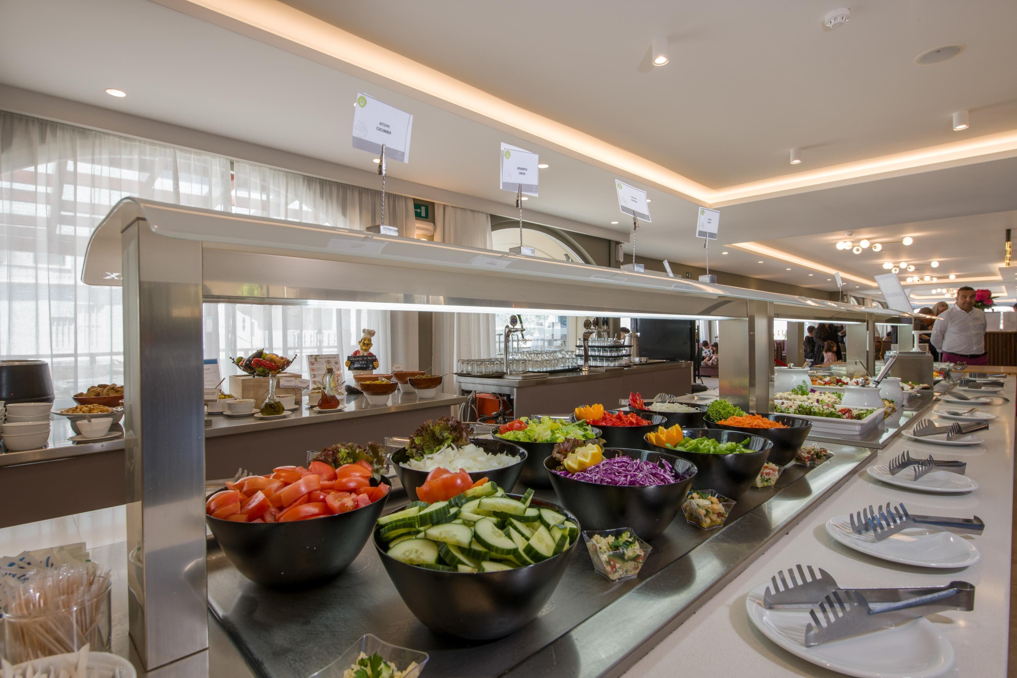 Un bufé con diversas opciones de comida, entre ellas ensaladas y verduras, en un moderno y bien iluminado hotel.