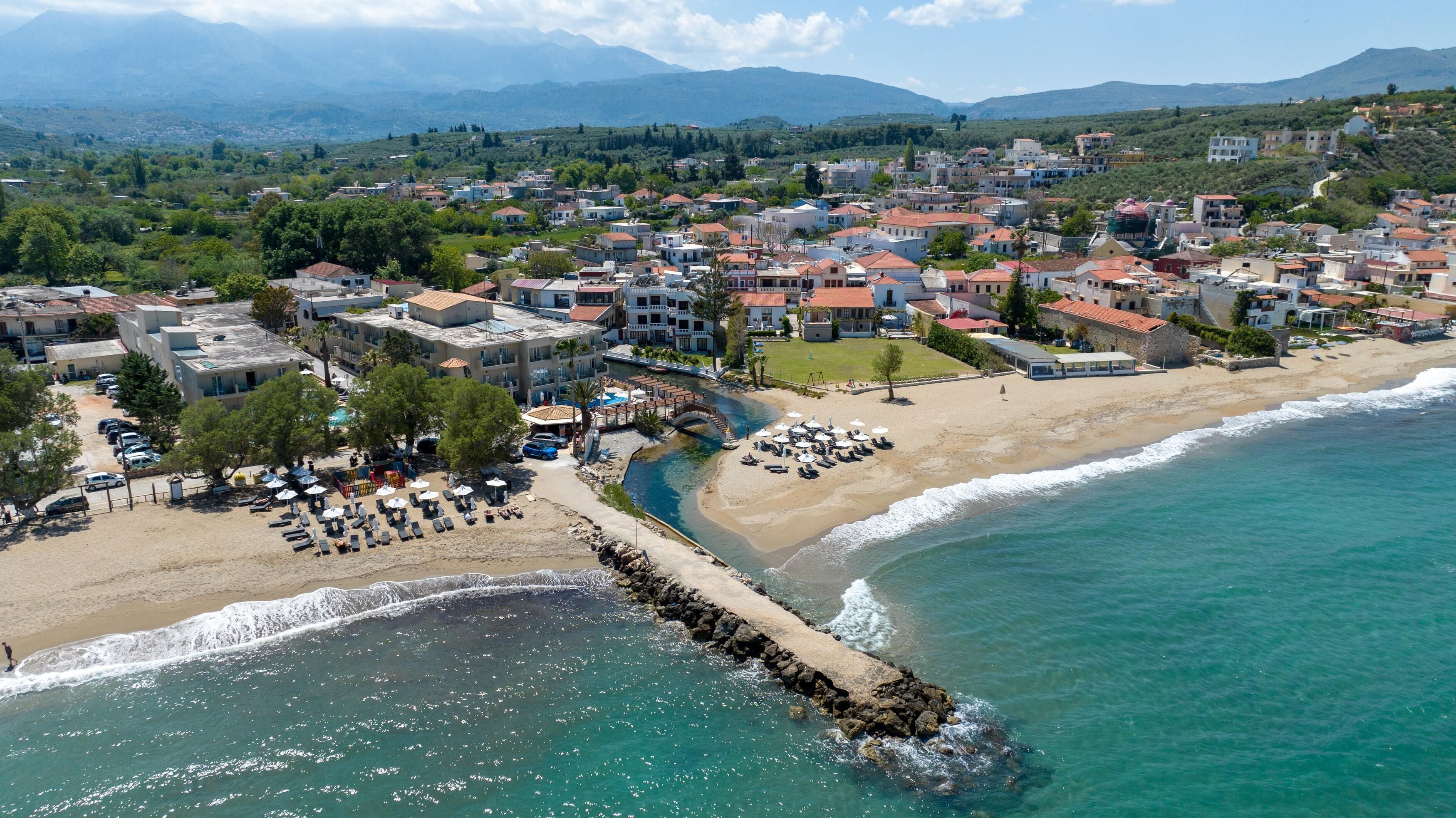 An aerial view of a coastal town with a beach, a marina, and a variety of buildings.