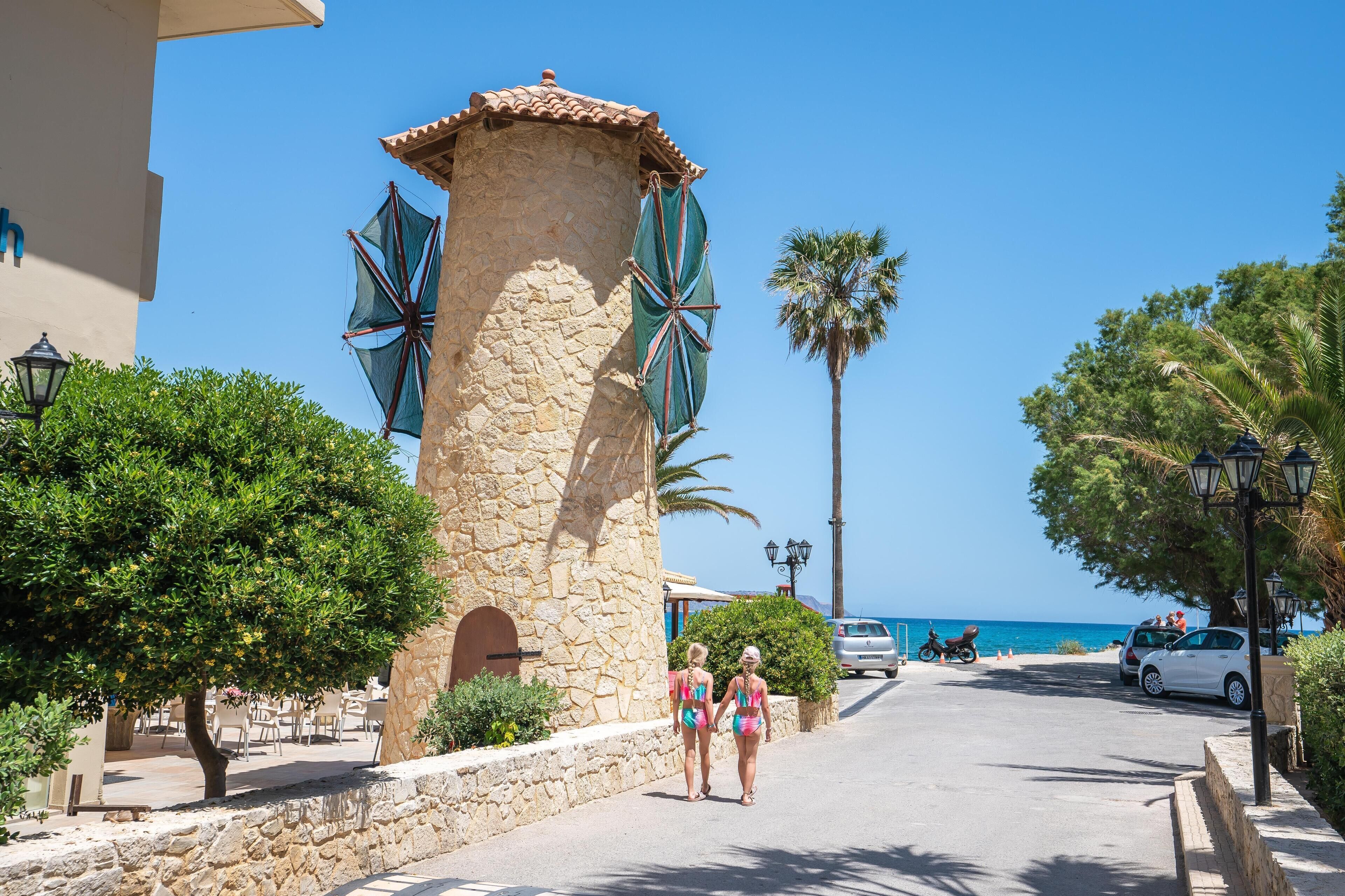 Una calle costera con edificios de piedra, palmeras y una vista despejada del mar.