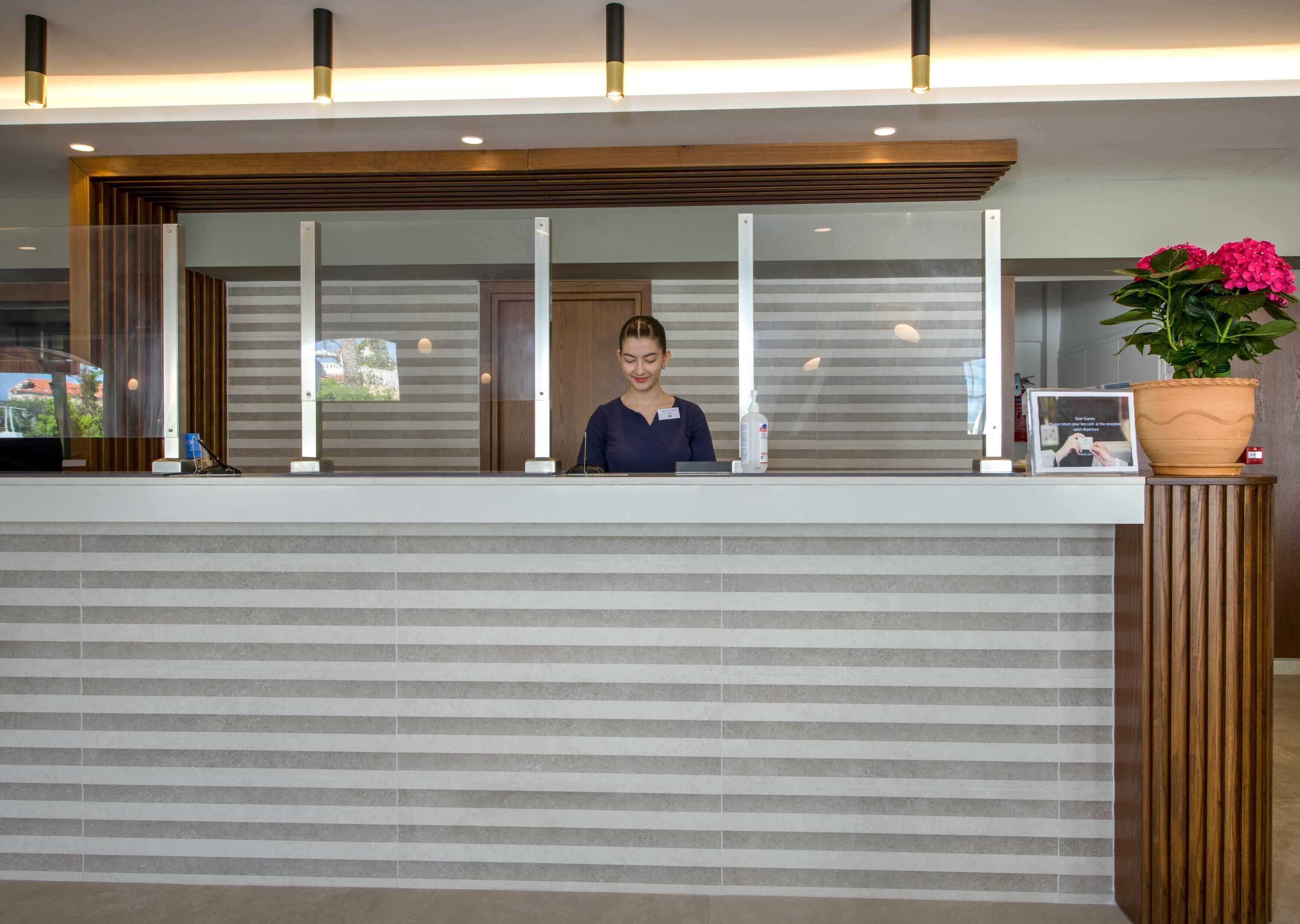 Una mesa de recepción con una pared a rayas, un recepcionista y una planta en maceta.