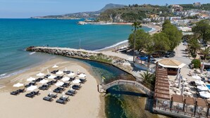 Una playa con tumbonas y sombrillas, un puente de piedra y una zona de piscina.