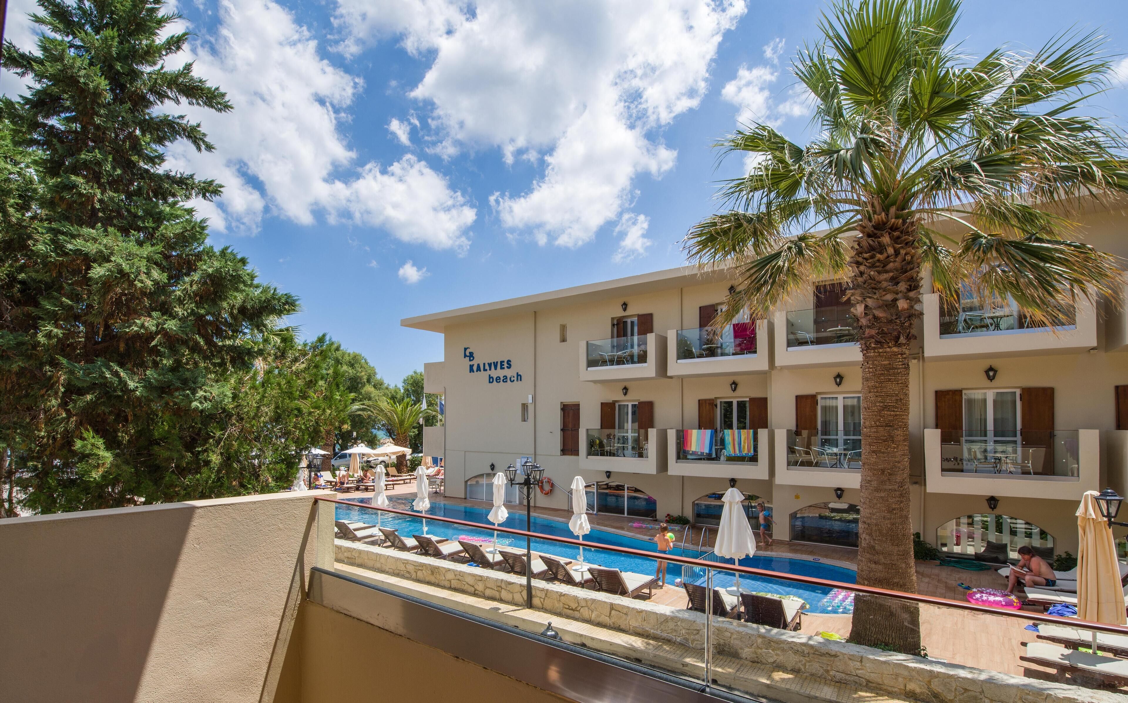 A hotel with a pool, outdoor seating, and a palm tree.