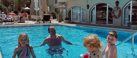 A pool area with a clear blue pool, a lifebuoy, and a building with a balcony.