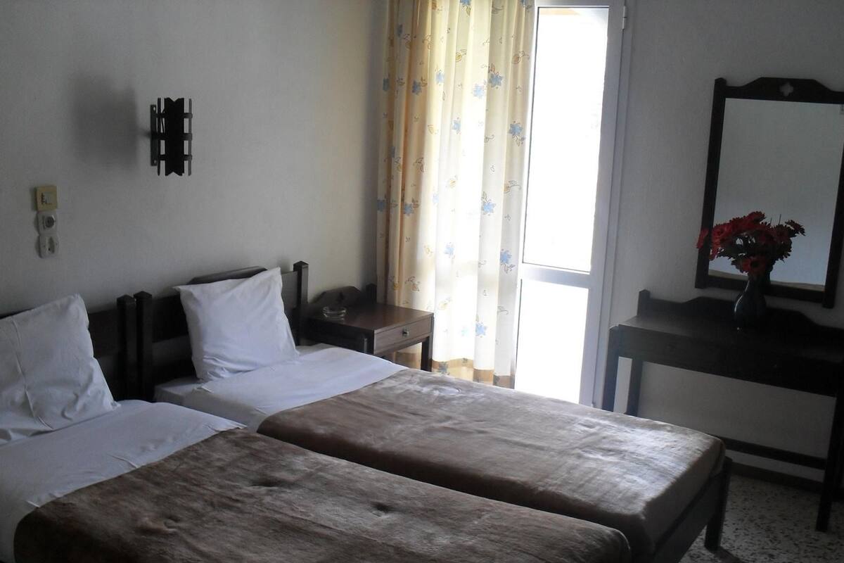 Ein Hotelzimmer mit zwei Betten, einem Schreibtisch, einem Spiegel und einem Fenster mit Vorhängen.