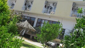A multi-story hotel with balconies, air conditioning units, and a thatched-roof structure in the foreground. - Armonia Hotel (Hersonissos)
