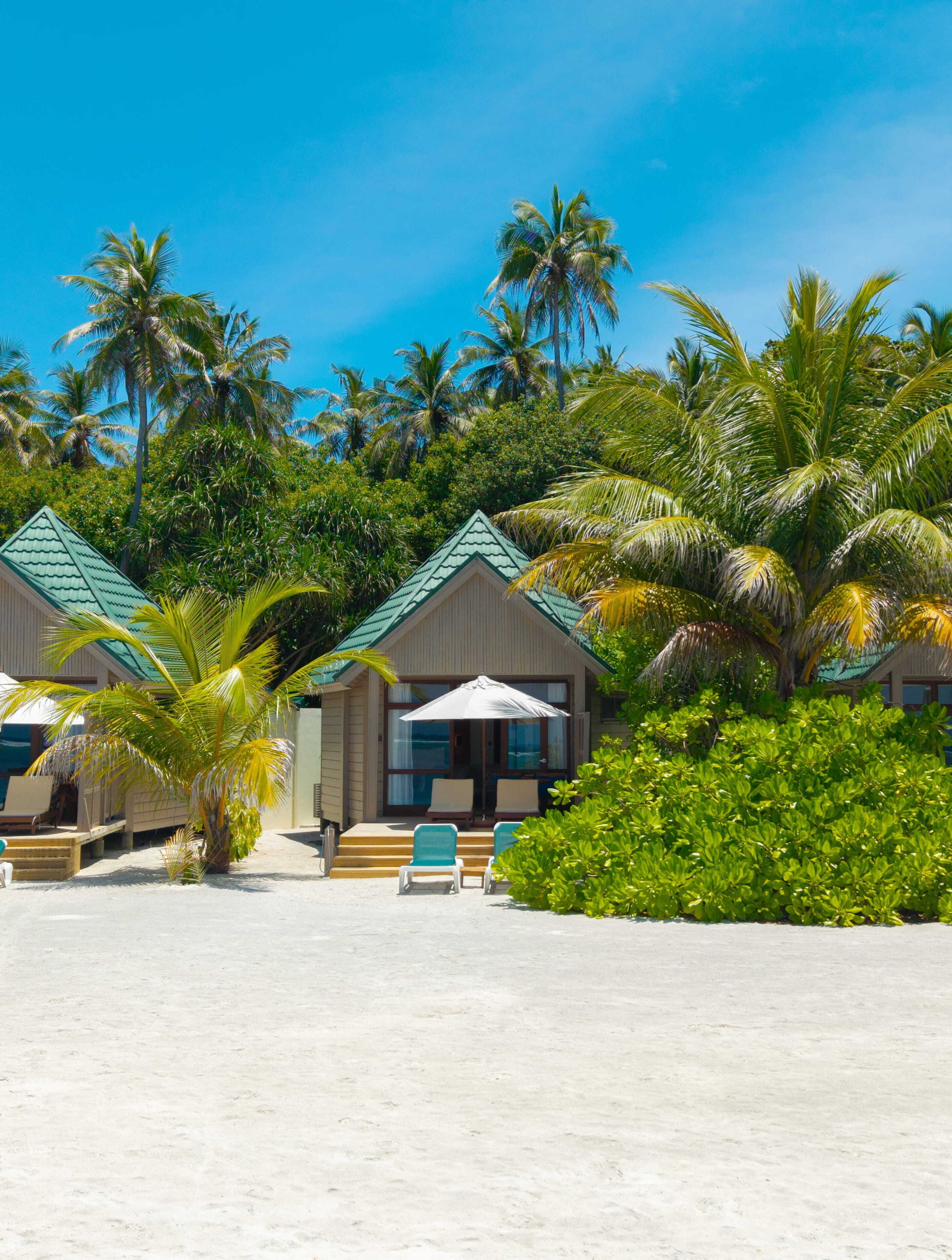 A beachfront property with multiple bungalow-style accommodations, each featuring a private entrance and a seating area with a table and chairs.