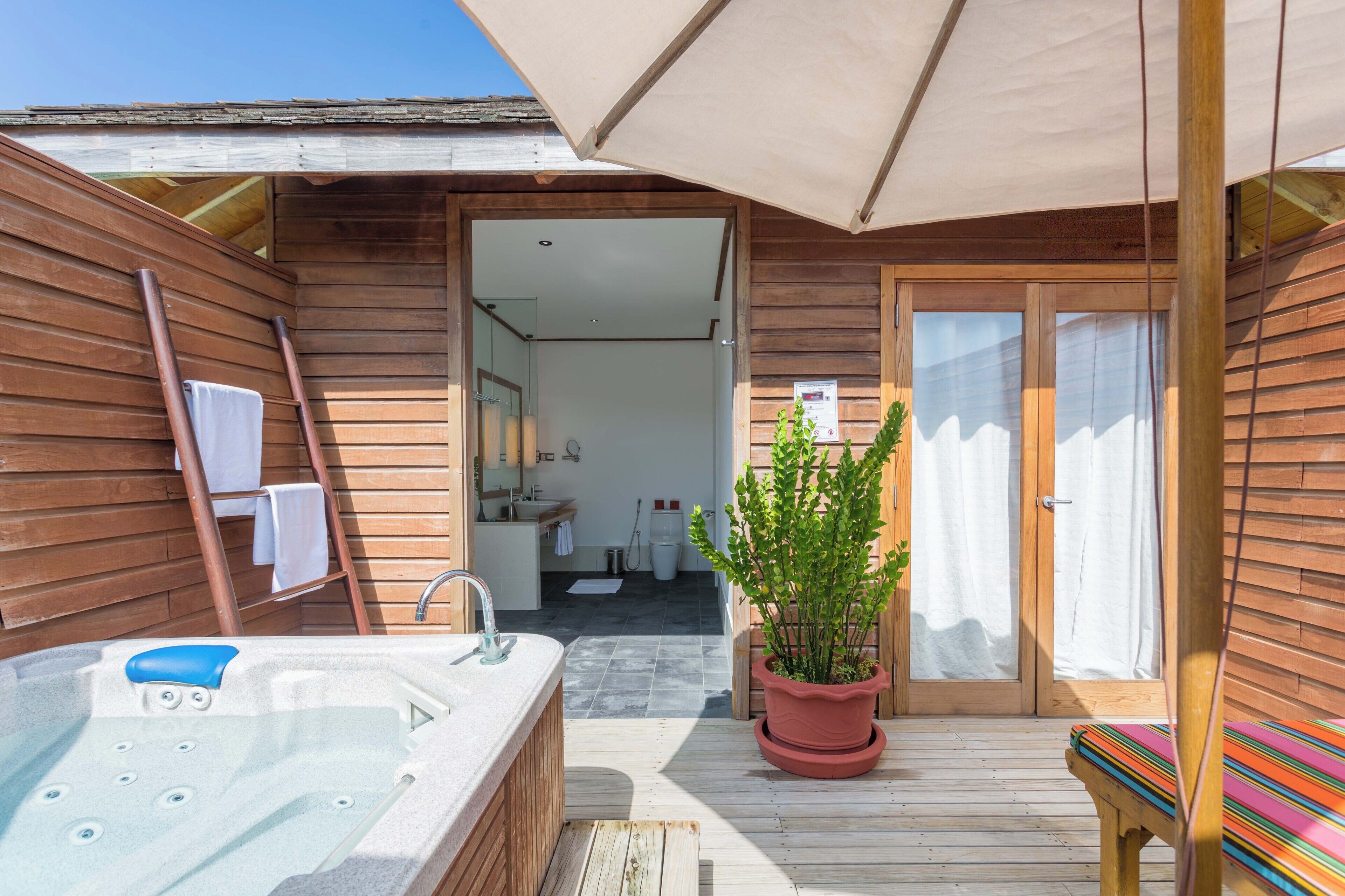 A wooden cabin with a hot tub, a bench, and a potted plant.