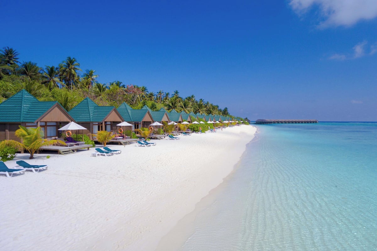 Un resort en la playa con bungalows sobre el agua, agua turquesa cristalina y una playa de arena blanca.