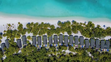 Eine Vogelperspektive zeigt ein Resort mit Reihen von Villen am Strand, einem Sandstrand und einem klaren türkisblauen Meer.