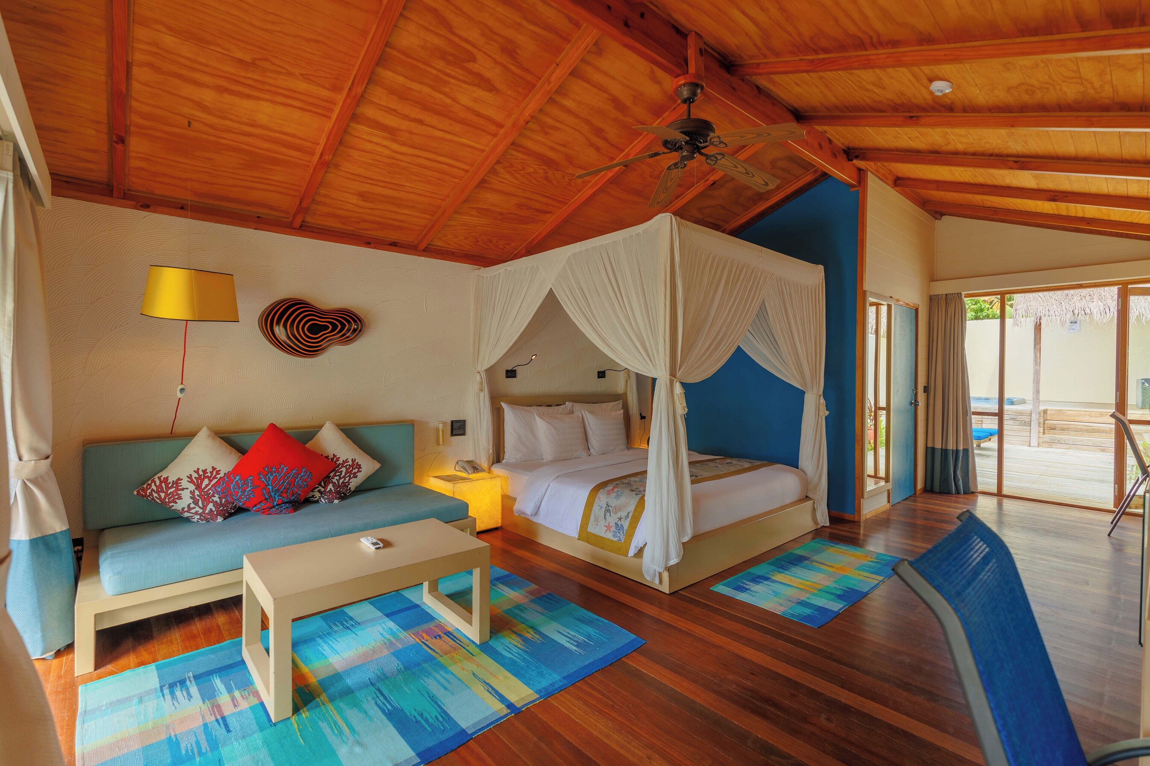 Een kamer met een bed, een slaapbank, een tafel en een plafondventilator.