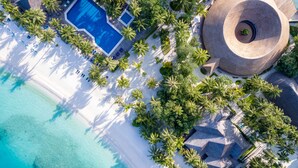 Vista aérea de un resort con piscina, palmeras y un edificio circular.