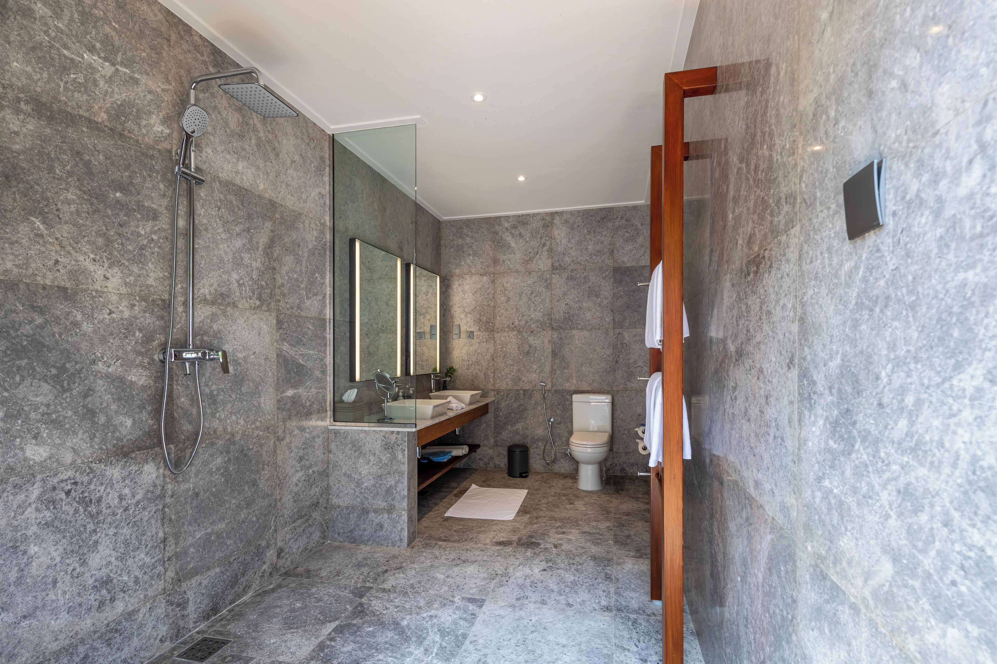 Une salle de bain moderne équipée d’une douche, d’un lavabo et de toilettes, avec des murs en marbre et un grand miroir.