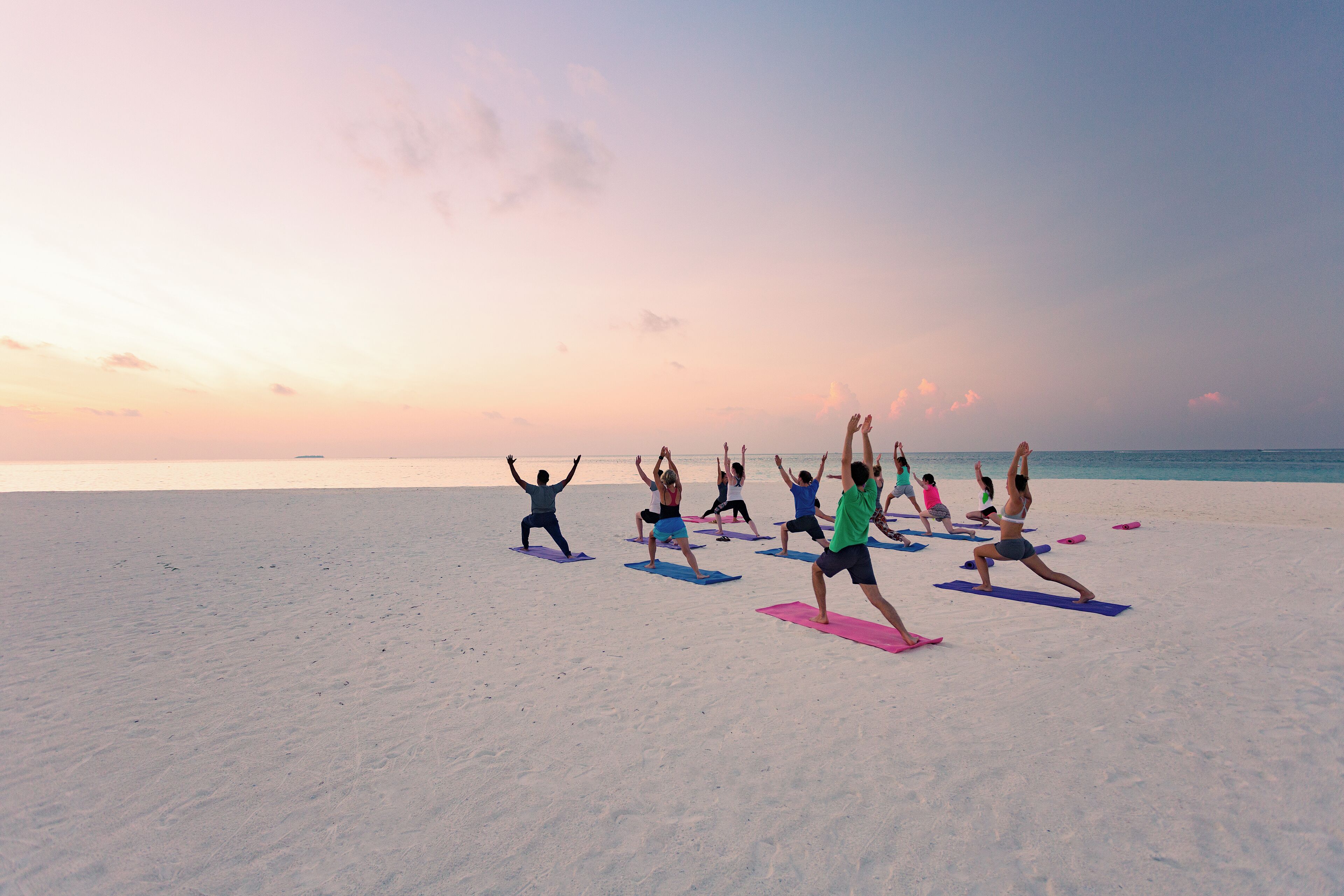 Un grupo de personas practicando yoga en una playa al atardecer.