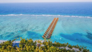 Cabañas sobre el agua alineadas en fila, extendiéndose hacia el océano, rodeadas de agua turquesa cristalina y palmeras.
