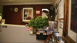 A reception area with a reception desk, a potted plant, a framed picture on the wall, and a sign with a logo. - Sunshine Motel (Fife)