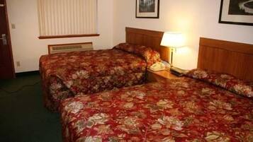 A hotel room with two beds, a bedside table with a lamp, and a window with blinds.