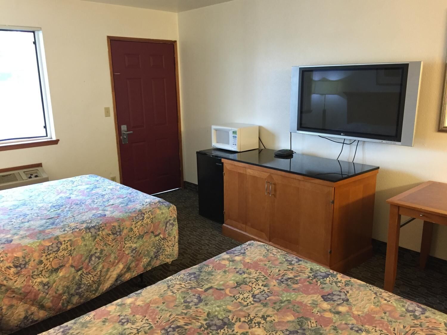 Habitación de hotel con dos camas, televisión, microondas y un pequeño escritorio.