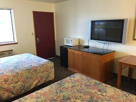Habitación de hotel con dos camas, televisión, microondas y un pequeño escritorio.