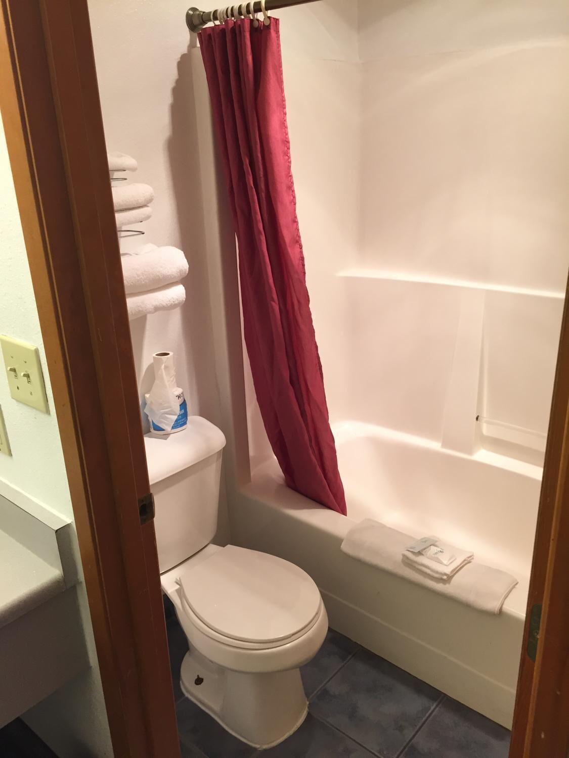 Une salle de bain avec des toilettes blanches, une baignoire et un rideau de douche rouge.