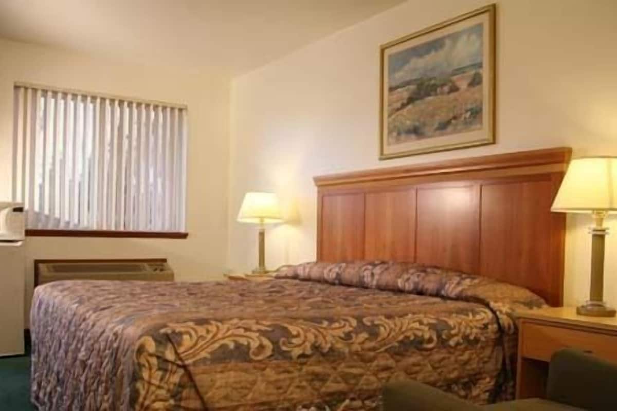 A hotel room with a bed, two bedside lamps, a desk with a chair, a television, and a painting on the wall.
