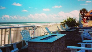 Un patio frente a la playa con sillas Adirondack blancas, una mesa de piedra y vista al océano.