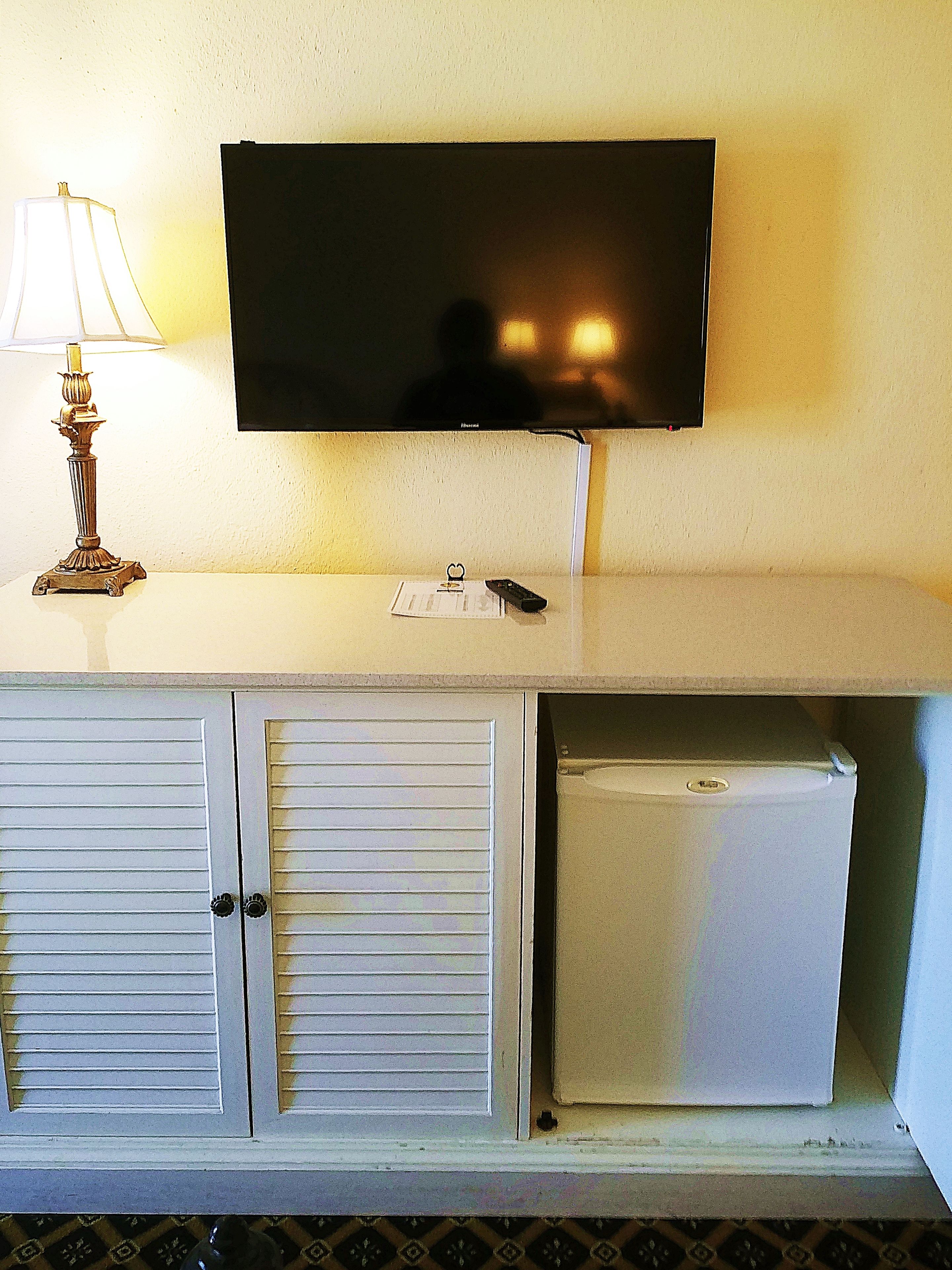 A television mounted on a wall above a white cabinet with two doors and a small refrigerator.