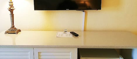 A television mounted on a wall above a white cabinet with two doors and a small refrigerator.