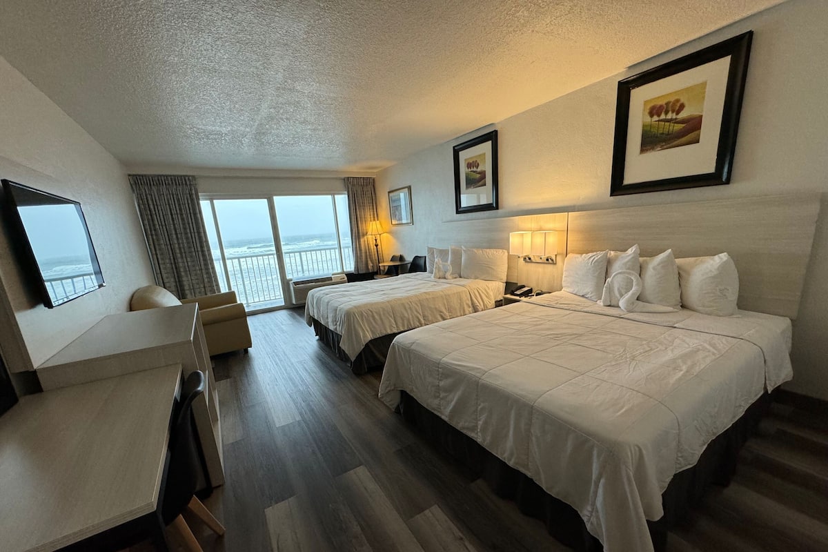 A hotel room with two beds, a desk, and a view of the ocean.