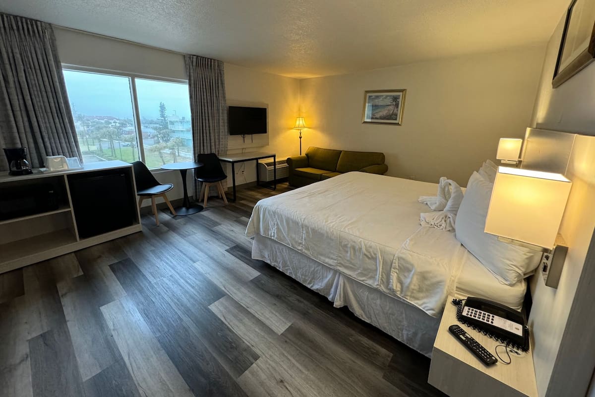 A hotel room with a bed, desk, chair, and a view of the city.