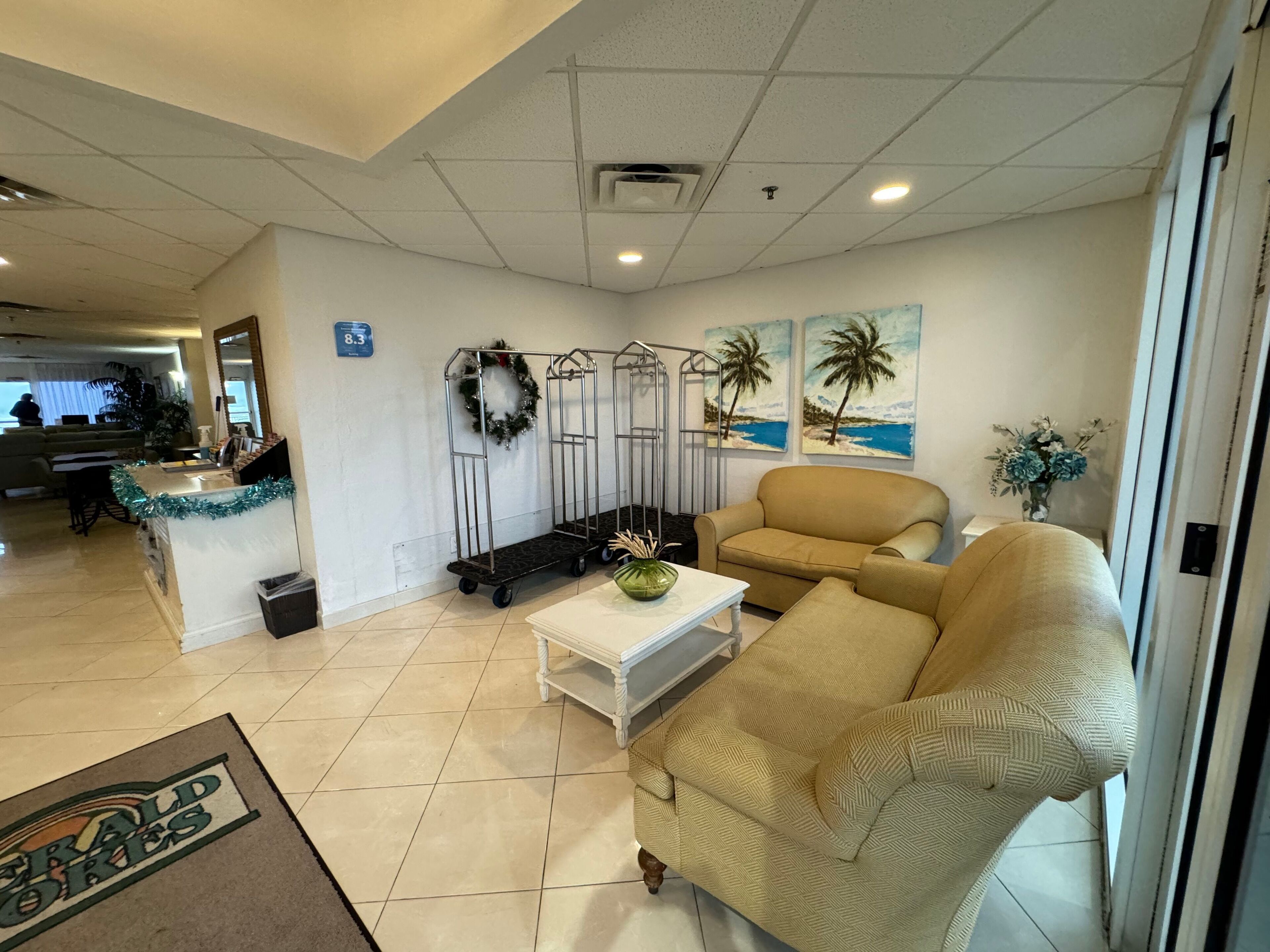 A hotel lobby with a reception desk, a beige sofa, a white coffee table, and a decorative wreath.