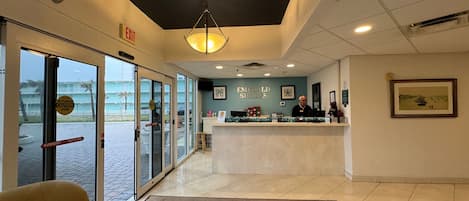 A hotel lobby with a reception desk, a large window, and a door with an emergency exit sign.