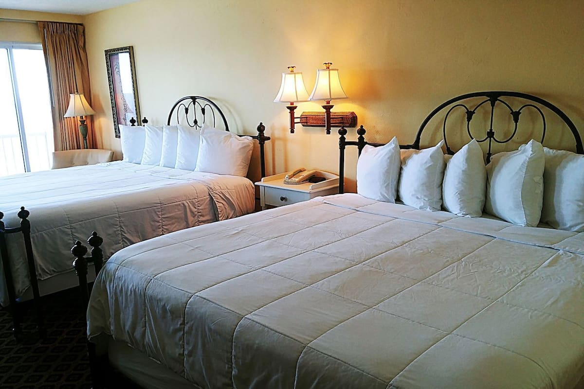 A hotel room with two beds, a nightstand, lamps, and a window with curtains.