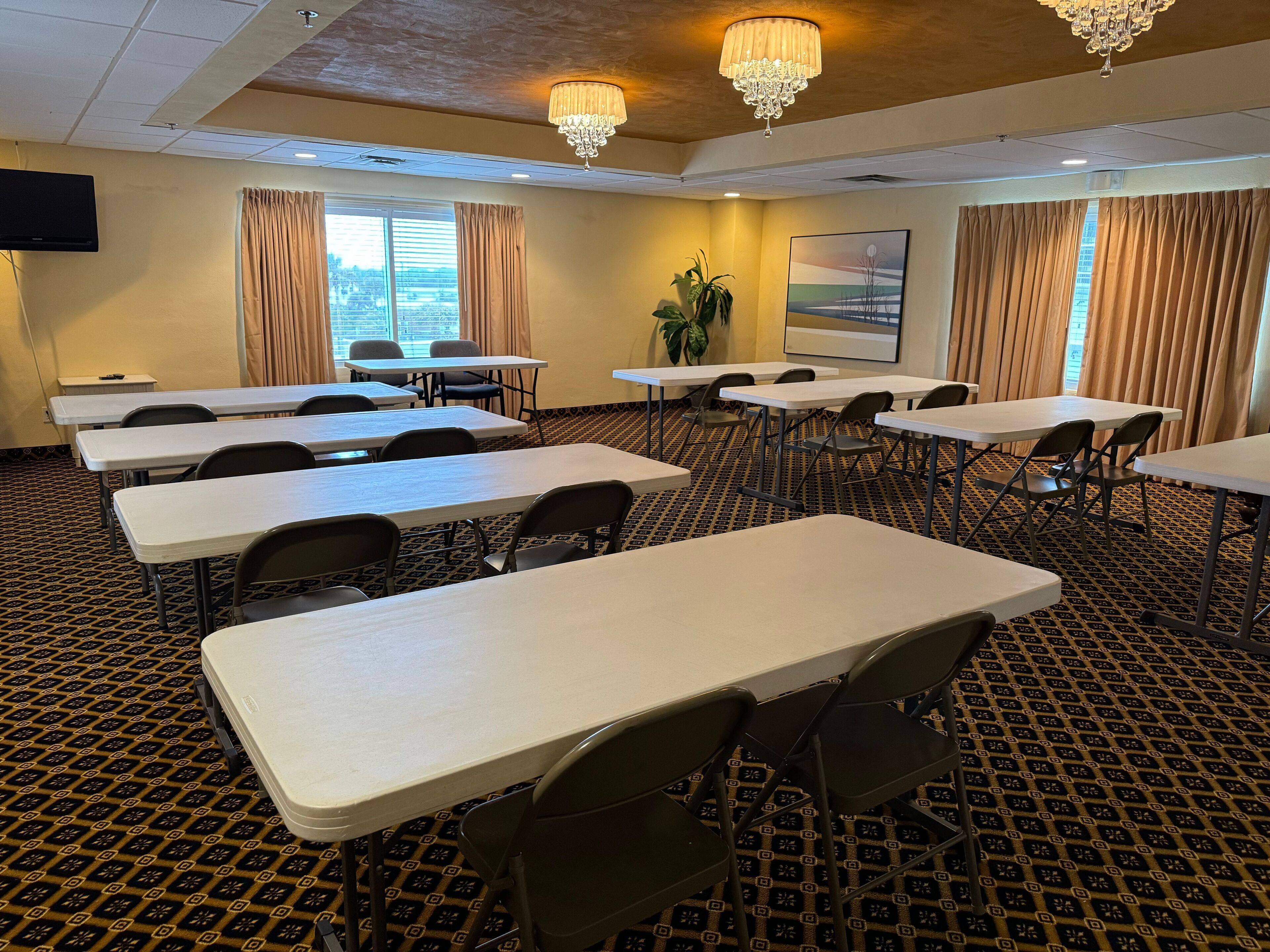 Ein Konferenzraum mit Tischen, Stühlen, einer Chandelier, einem Fernseher und einer Pflanze.