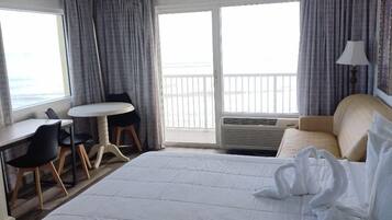 Habitación de hotel con una cama grande, un escritorio, dos sillas, un balcón con cortinas y una lámpara.