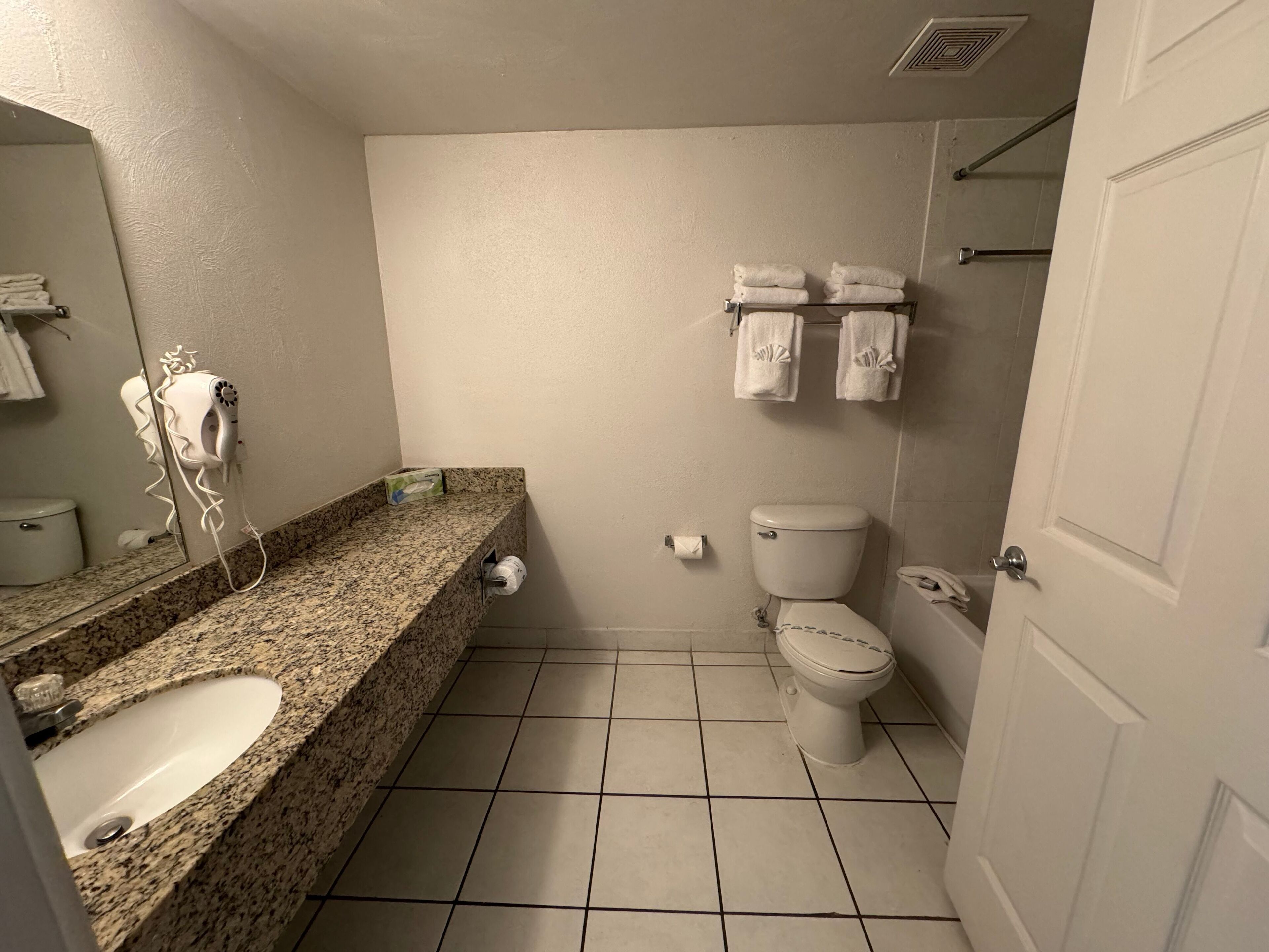 Un baño con encimera de granito, un lavabo, un inodoro y un perchero con toallas.