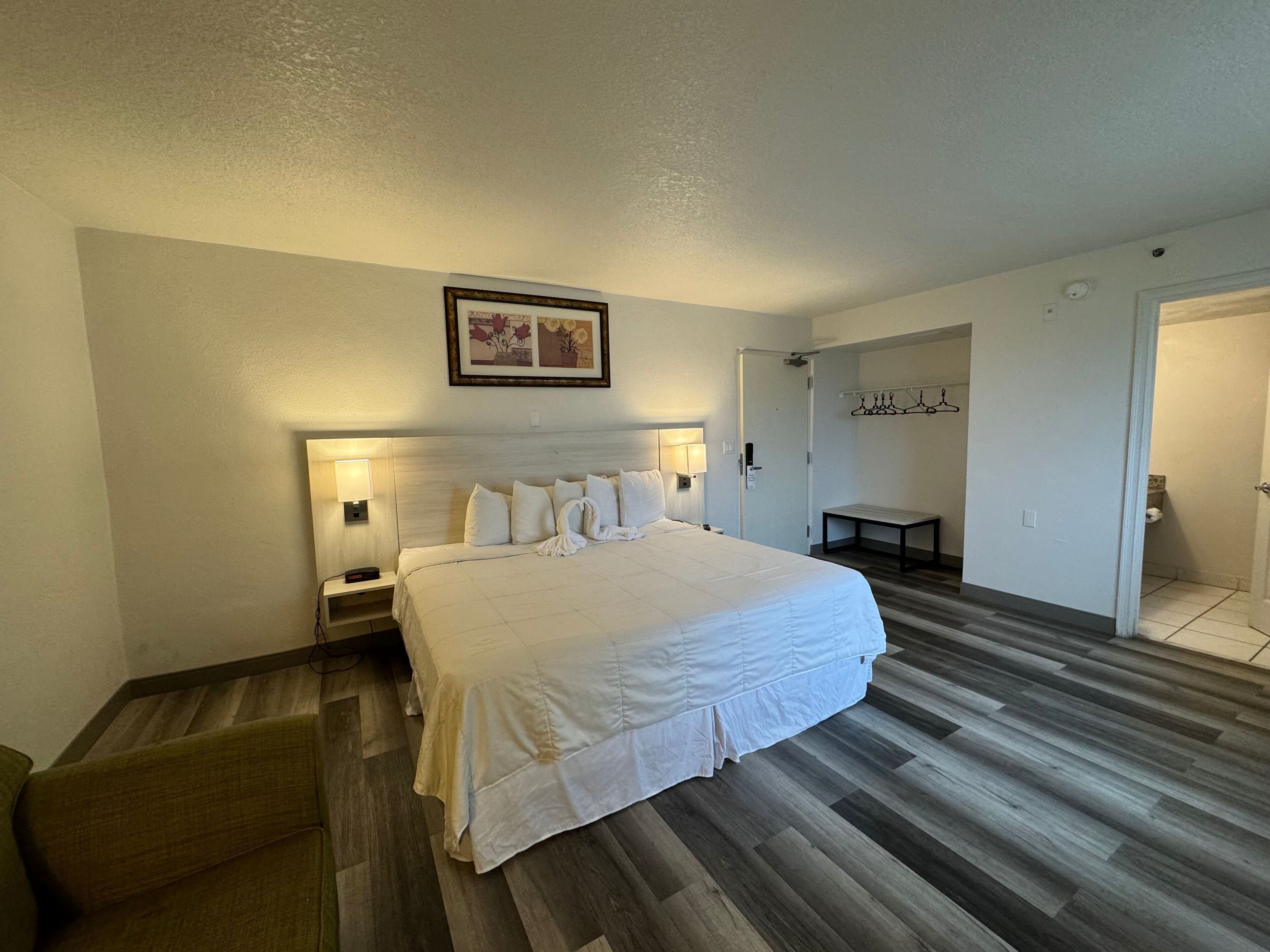 A hotel room with a large bed, bedside lamps, a wooden floor, a bench, and a coat rack.