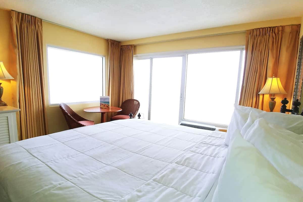 A hotel room with a large bed, a small round table, two chairs, and a window with curtains.