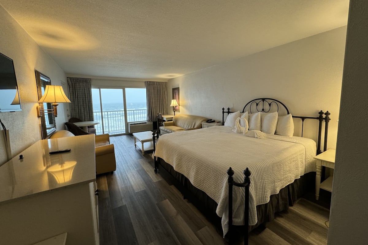 A hotel room with a large bed, a desk, a chair, and a view of the ocean.