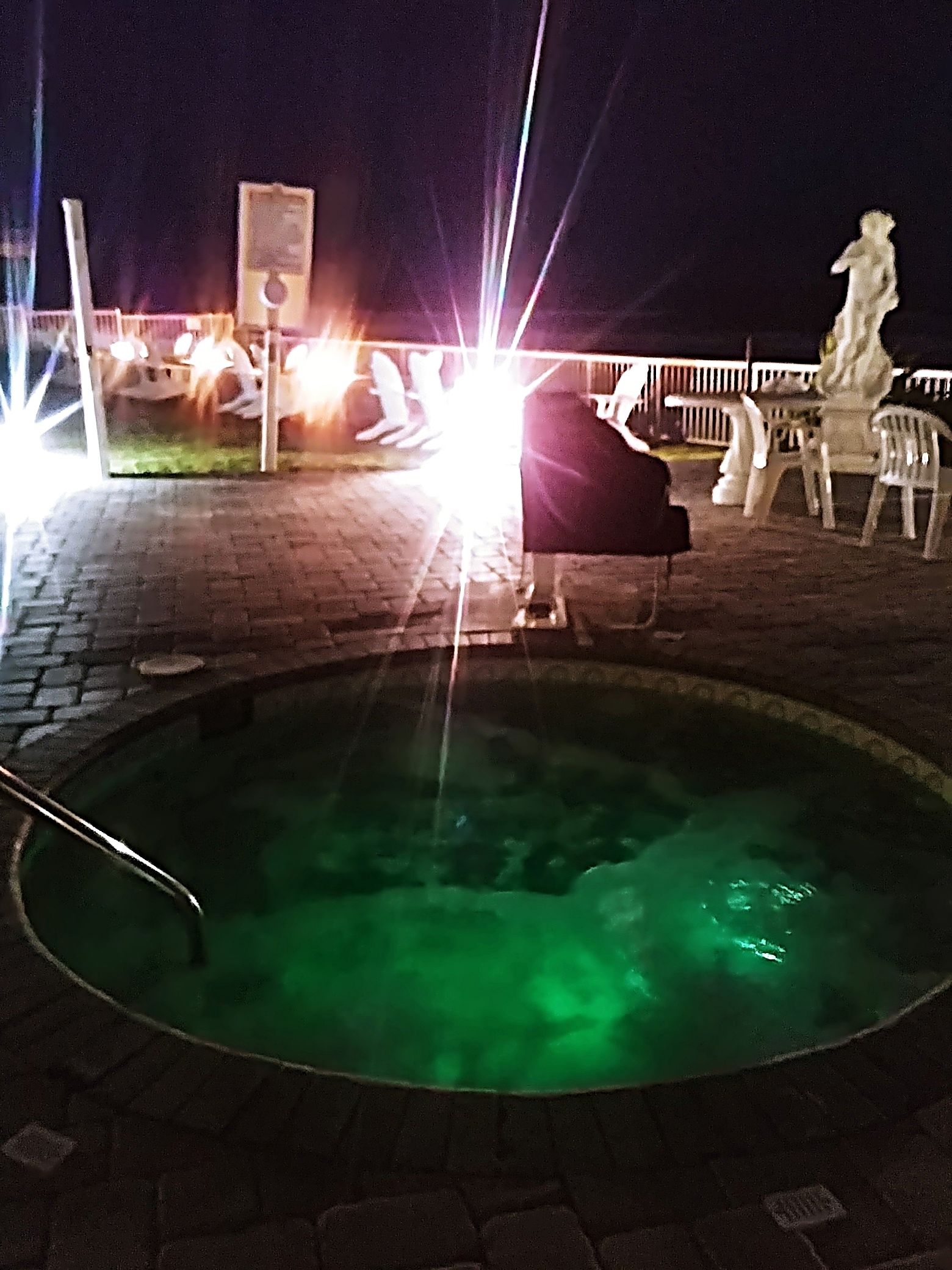 A hot tub with green lighting, surrounded by a brick patio.