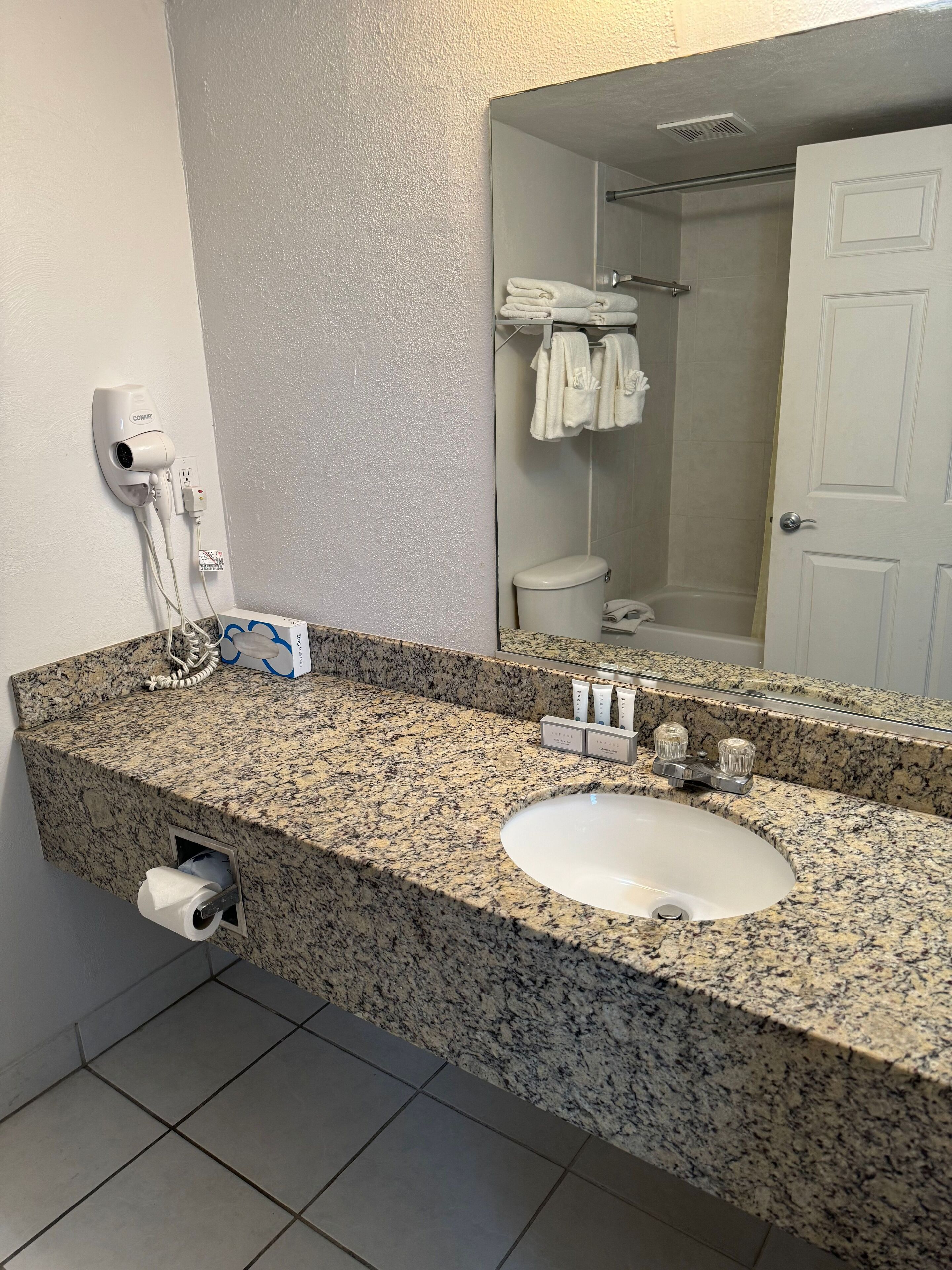 A bathroom with a granite countertop, a white sink, a hairdryer, and a towel rack.