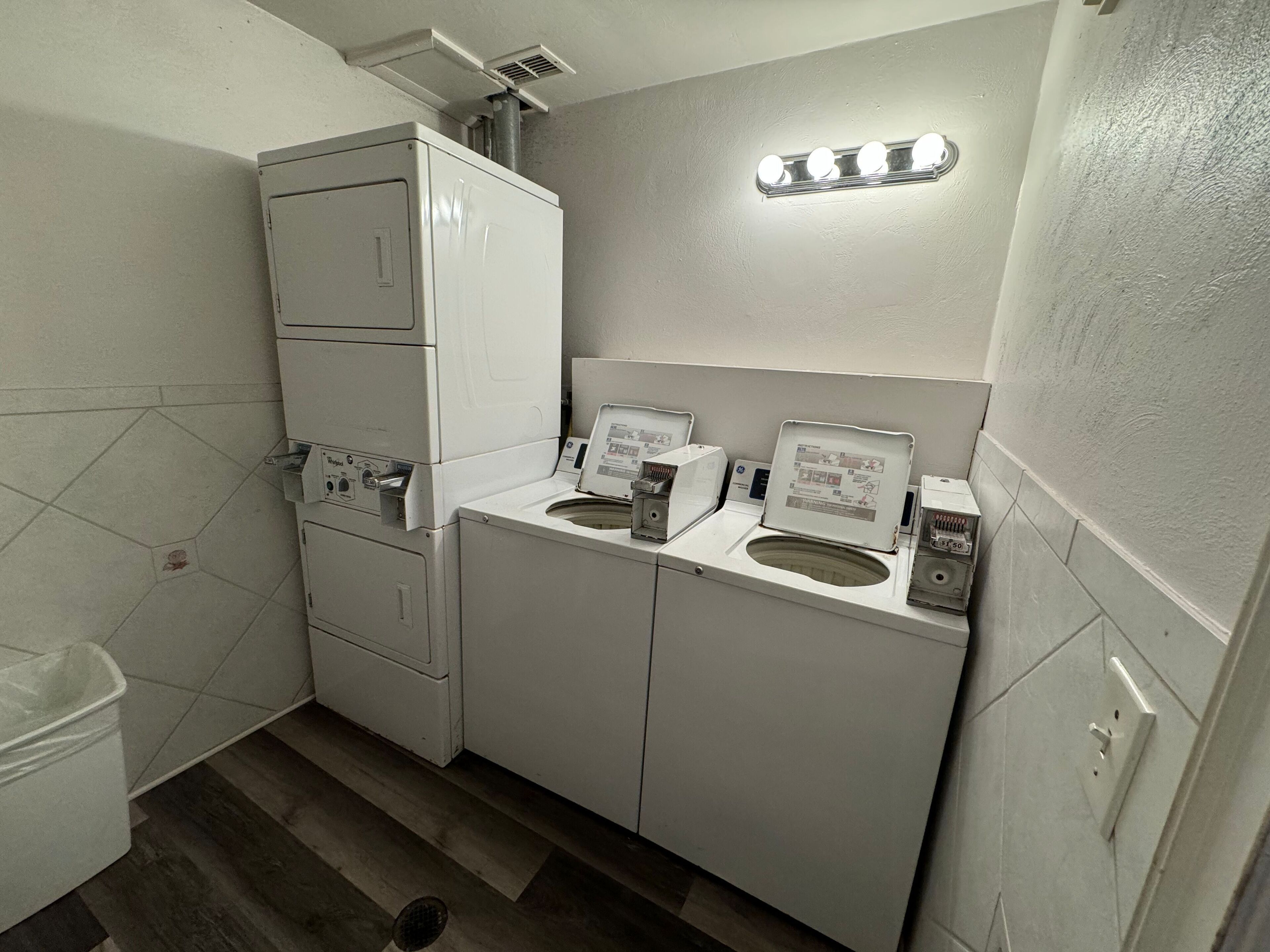 Un lavadero pequeño y funcional con lavadora y secadora apiladas, un lavabo y un espejo con luces arriba.