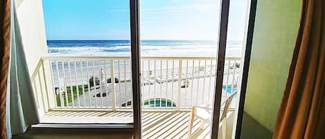 A balcony with a view of the ocean and a pool area.